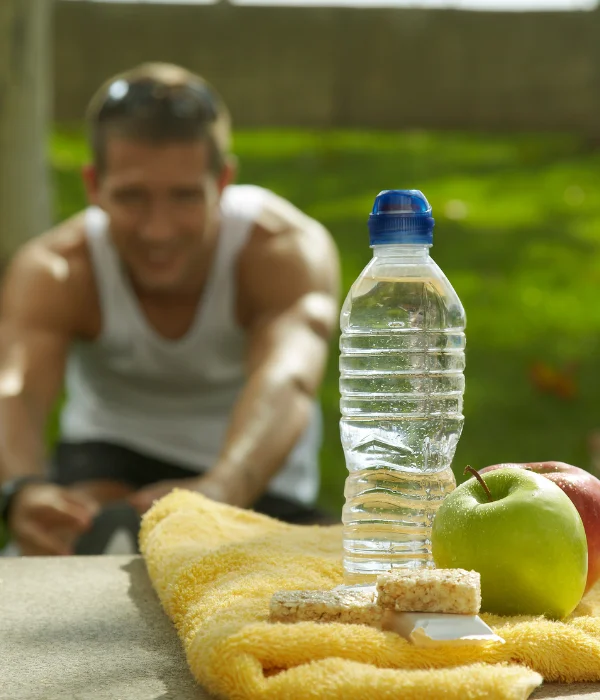 A man stretches with a water bottle and a couple apples next to him.